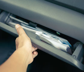 Mano abriendo la guantera de un coche con documentos