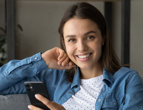 Mujer sonriente sentada en el sofá utilizando un smartphone