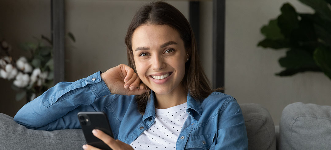 Mujer sonriente sentada en el sofá utilizando un smartphone