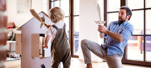 padre e hijo jugando en casa con espadas de cartón