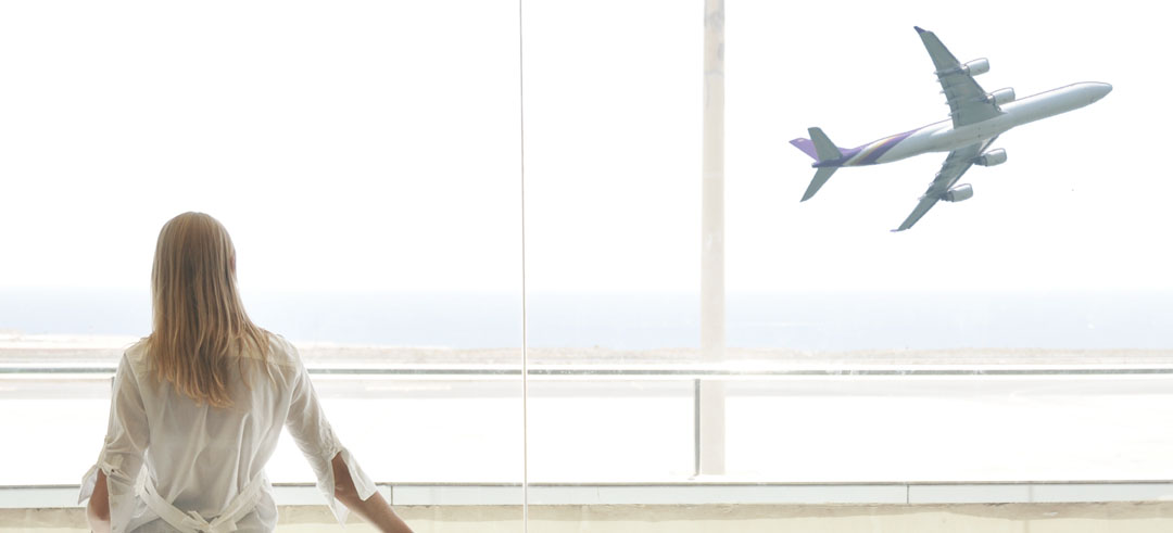 Mujer mirando por la ventana de un aeropuerto mientras despega un avión